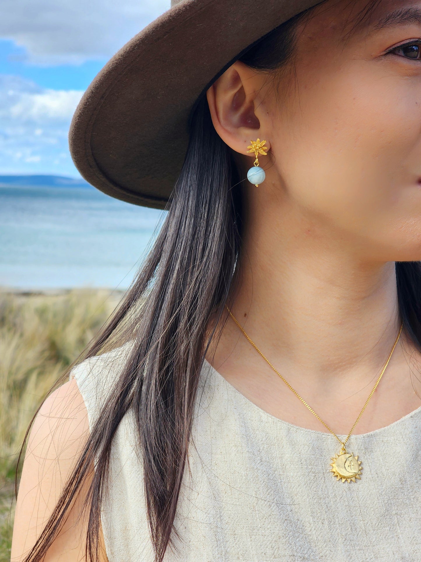 Hand sculpted aquamarine flower earrings in 18k gold vermeil, worn on model to show scale against a rugged, botanical Tasmania backdrop.
