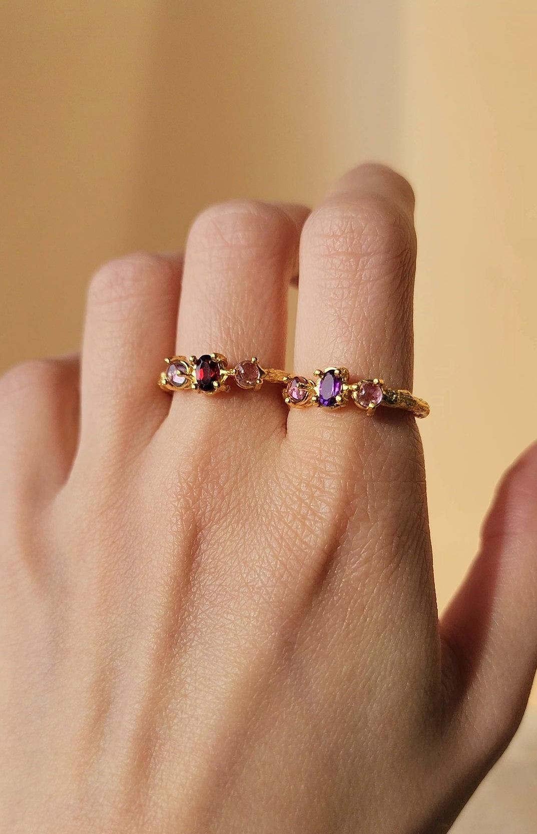 Triple stone ring featuring natural garnet and amethyst, hand crafted in 20k gold plated over solid recycled brass. Shown up close to highlight the organic molten textures of the organic double gallery basket set gemstones. 