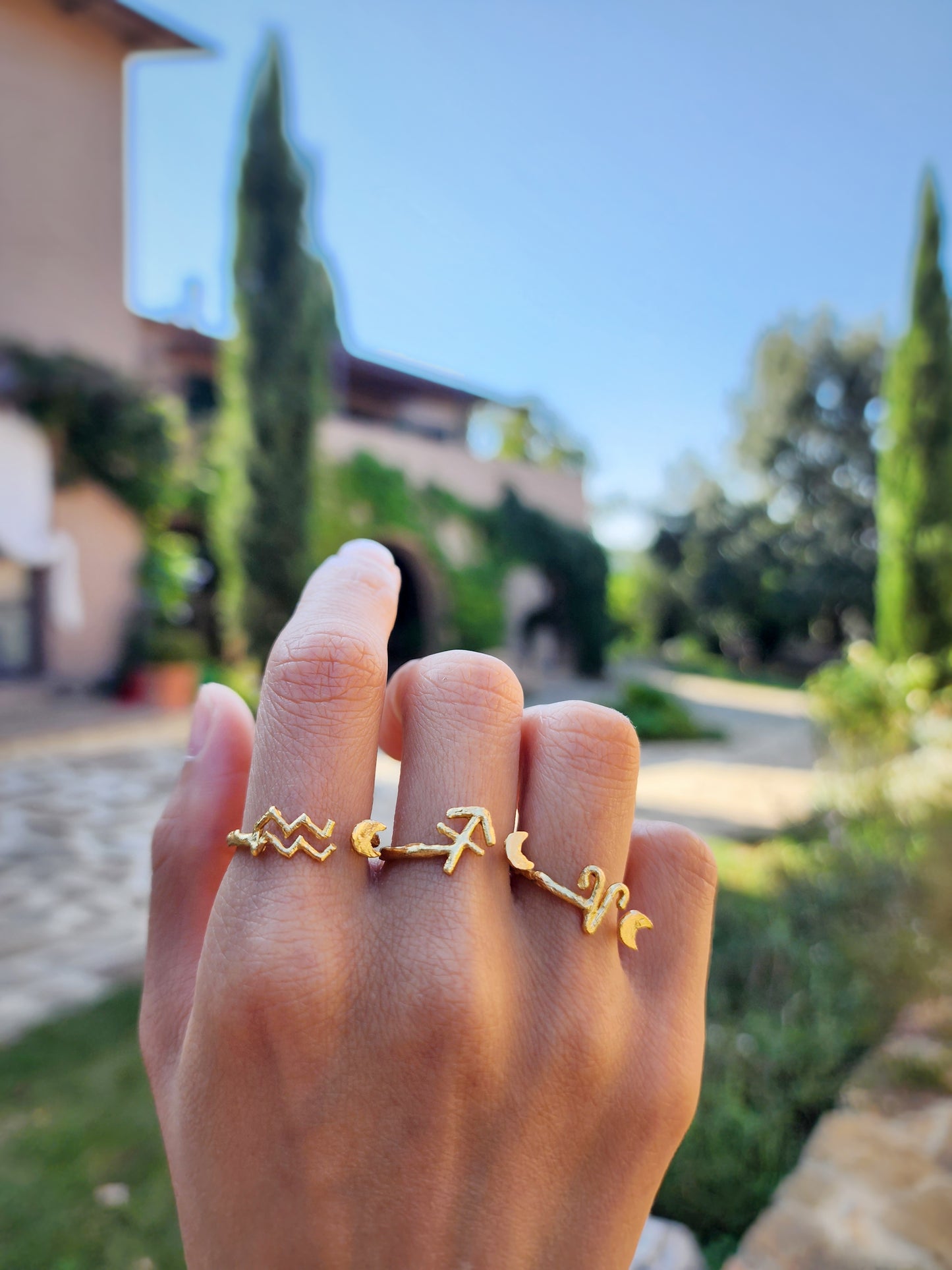 ​Three textured adjustable astrology sign rings in 18 ct thick gold plated brass, styled against the lush greenery of a Tuscany villa garden. These Sydney made pieces are photographed in the heart of Italy to reflect the brand's classical and celestial inspirations.