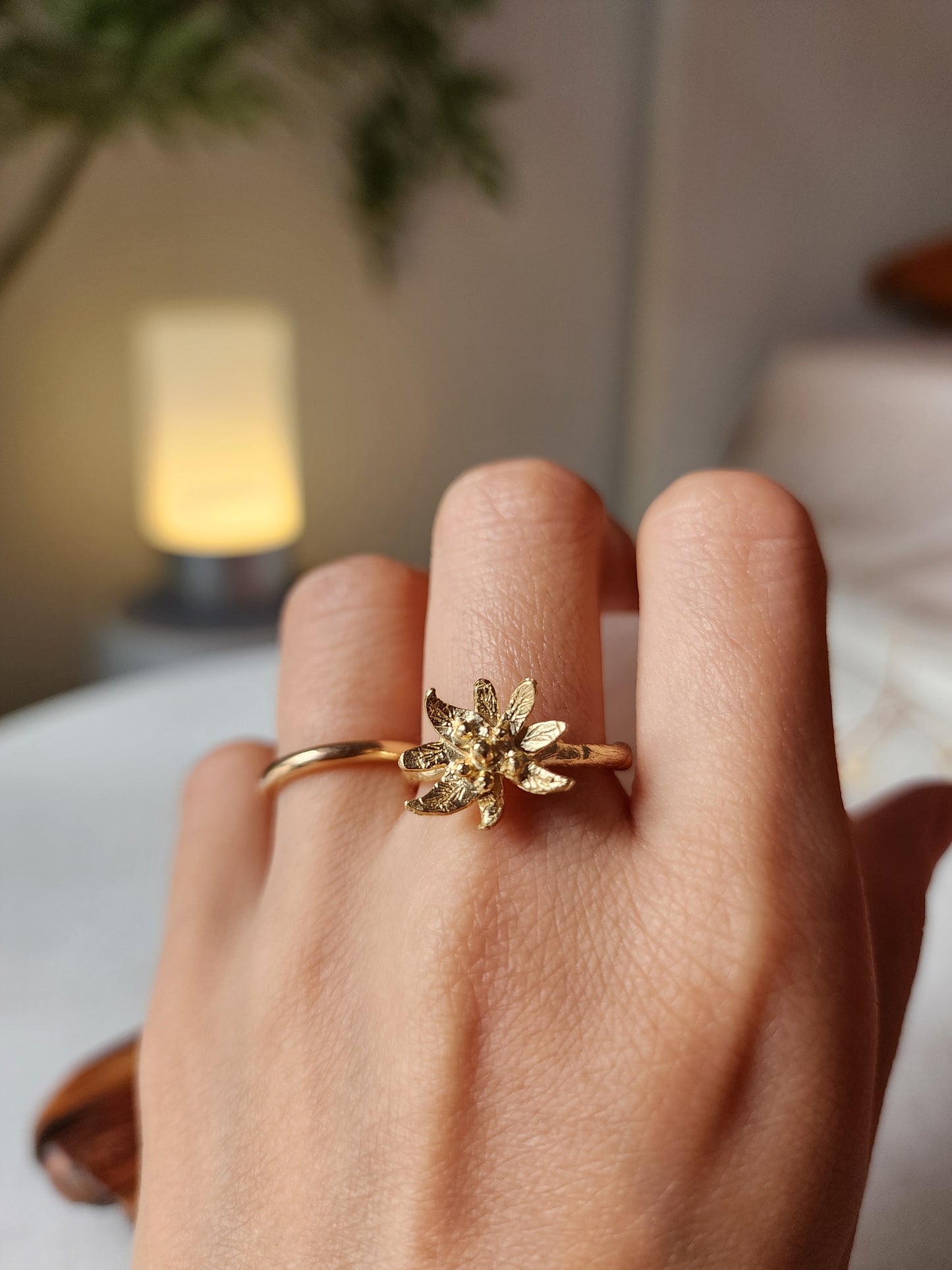 Edelweiss flower ring in 18k fine gold plating over recycled solid brass, worn on hand to showcase scale and size of the ring. Styled stacked with a wedding band to appeal to women looking for botanical jewellery to pair with wedding bands.
