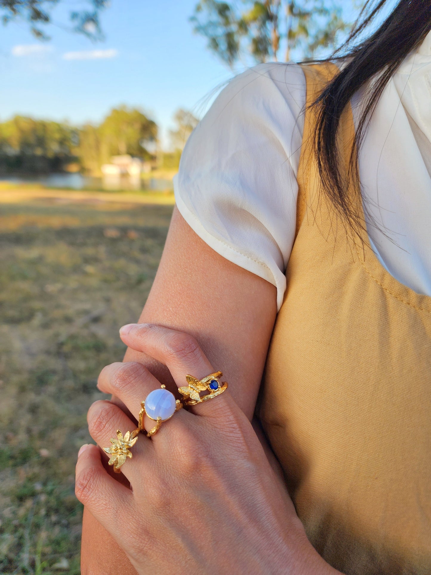 Gold Edelweiss flower ring shown worn with natural blue lace agate and sapphire butterfly gemstone rings. Photographed in an Australian bush setting.