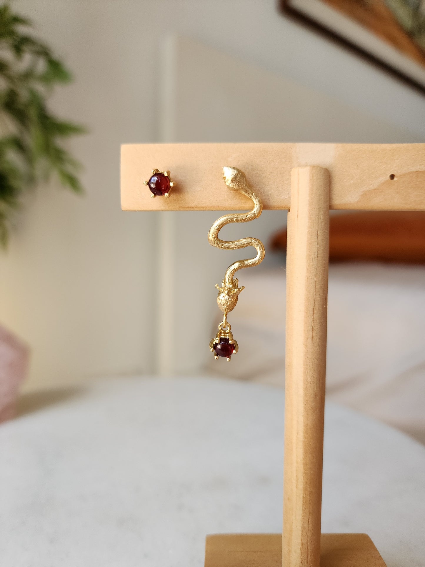 One of a kind red garnet earrings featuring snakes and stawberry. Asymmetrical style and displayed on a wooden jewellery stand. 