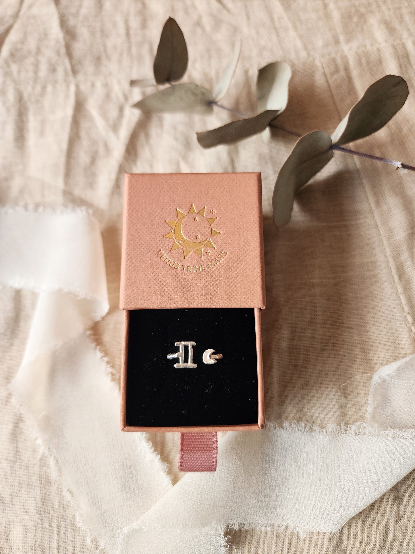 Gemini zodiac star sign ring, made in sterling silver and displayed in a terracotta coloured gift box, highlighting the ring as a gift for women born in May or June with the Gemini astrology sign. Styled with a beige linen cloth with a white silk ribbon and dried eucalyptus leaf to showcase the organic inspiration behind the handmade ring.