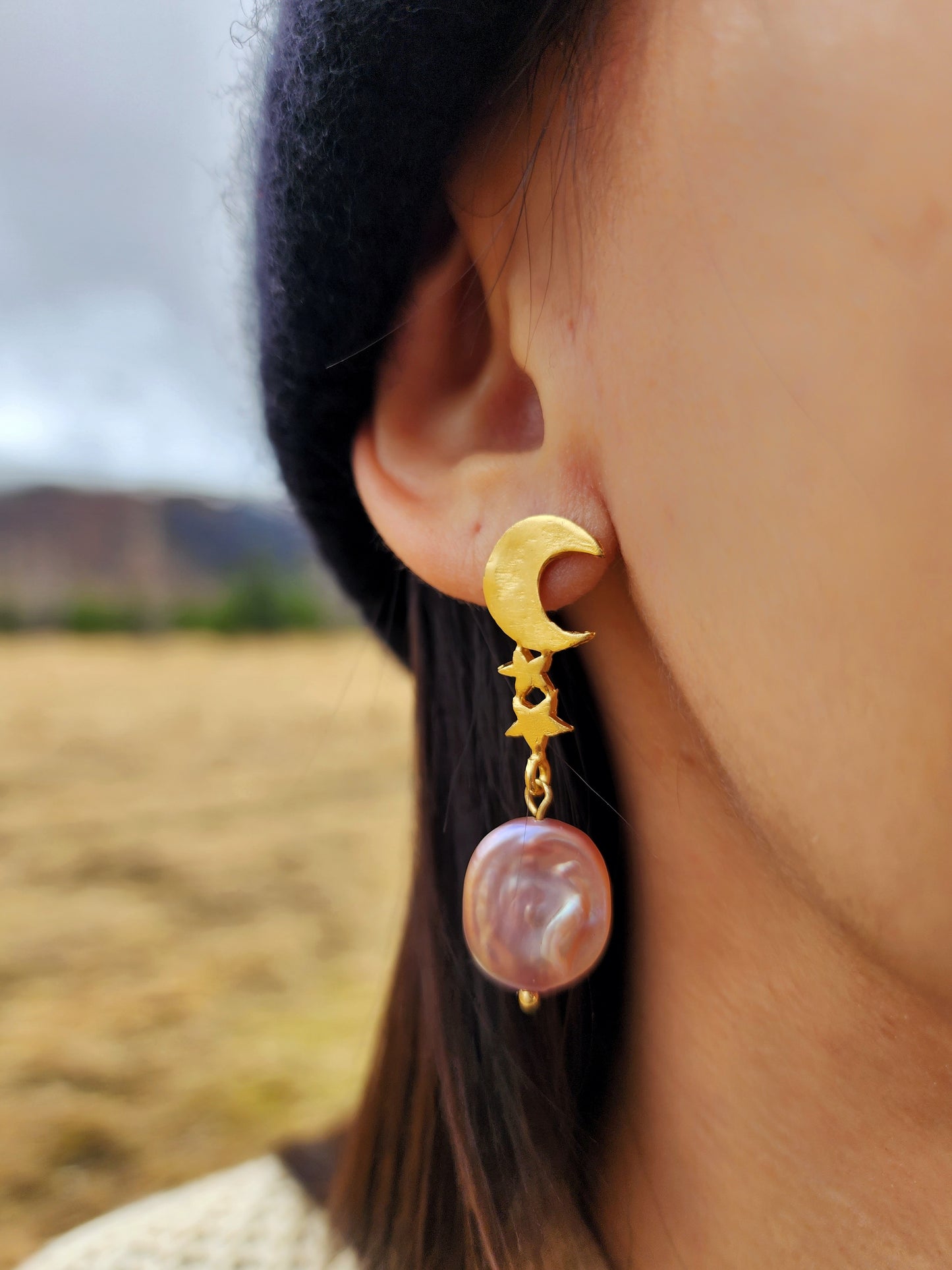 A hand sculpted celestial earrings featuring a pink pearl and moon and stars. Crafted in Sydney with gold vermeil and photographed against a raw Icelandic landscape. 