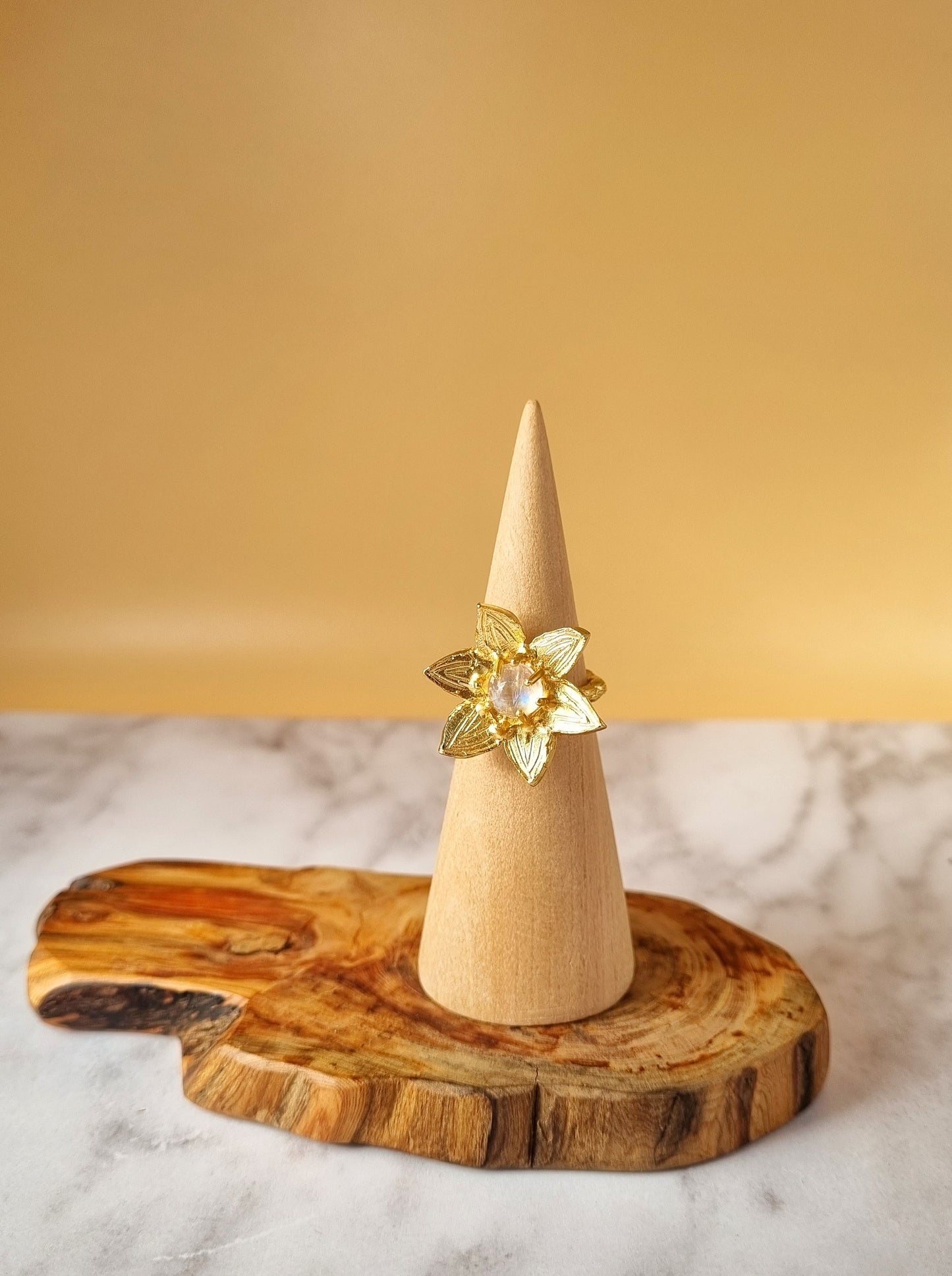 Moonstone flower ring, hand sculpted using the ancient lost wax technique and cast with recycled brass and finished with 18k fine gold. Statement ring shown on a ring stand and styled with a wooden display to highlight botanic inspiration. 