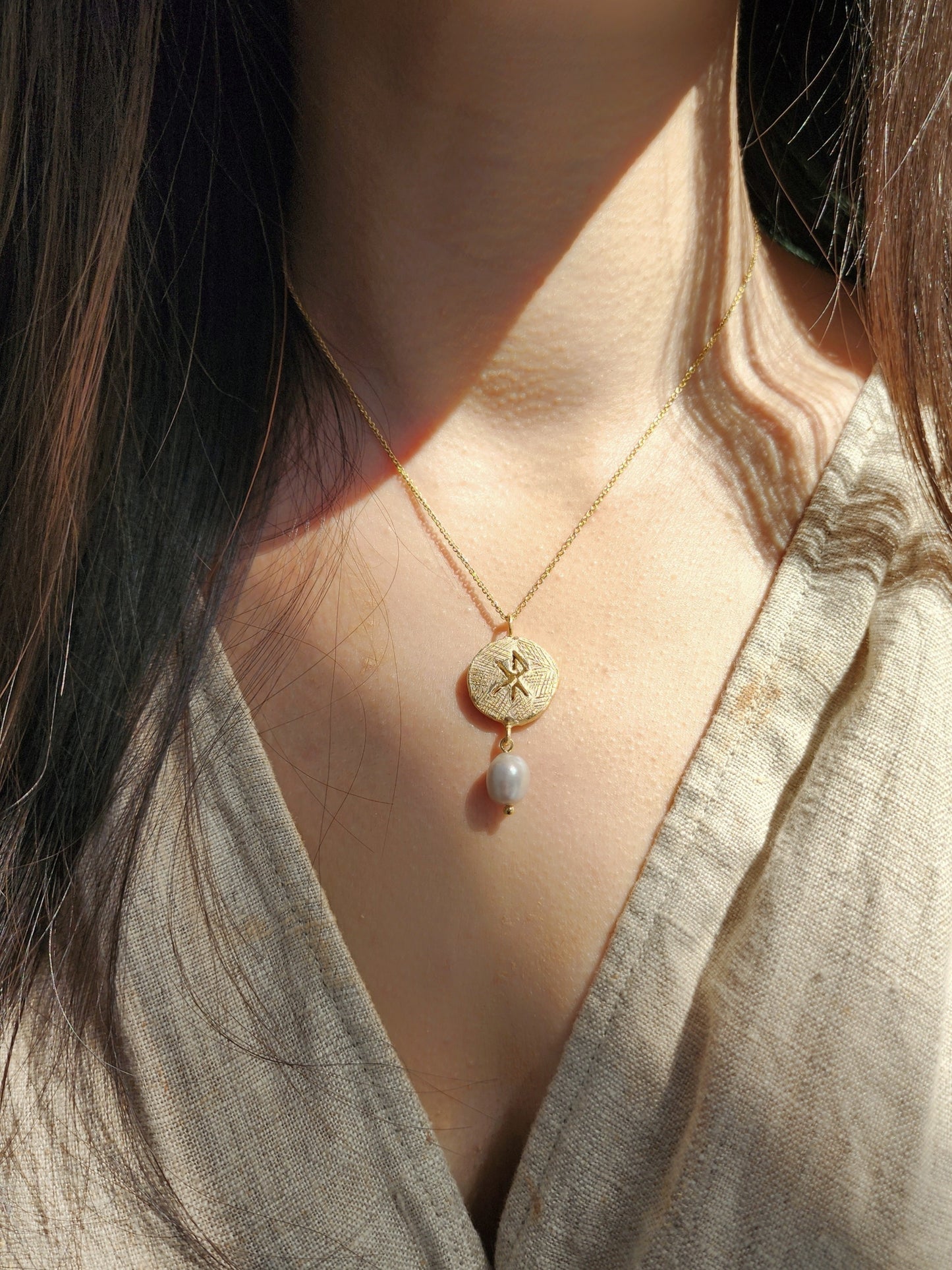 Viking inspired hand sculpted necklace featuring the norse symbol for love with a grey natural pearl. Worn on mode and styled with line taupe dress to show scale and glow from the 18k gold vermeil. 