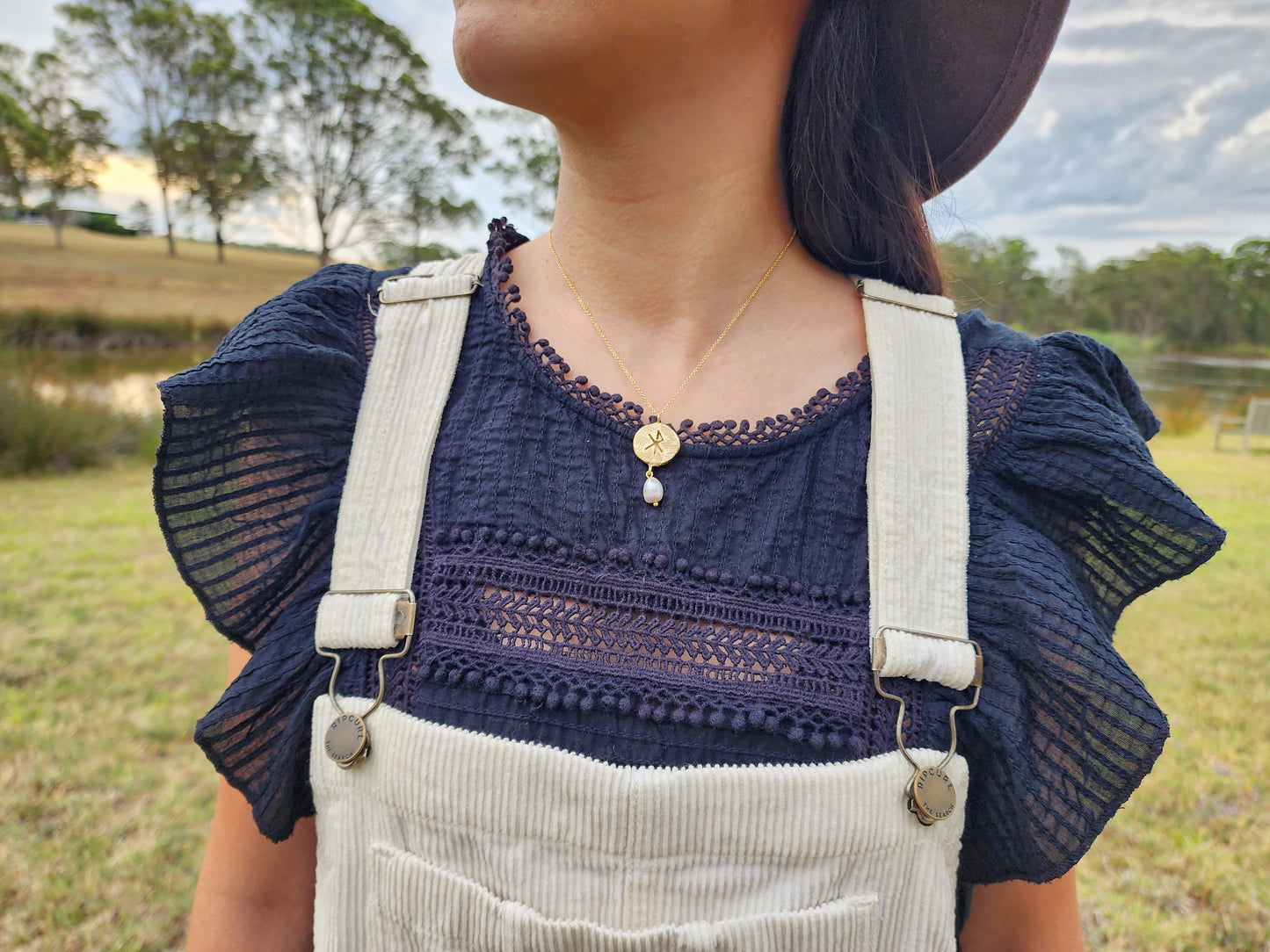 Hand sculpted necklace made from the lost wax casting process, crafted in Sydney that features the viking symbol of love. A freshwater grey pearl dangles below. Styled with a cotton black blouse and white overalls and photographed in an Australian bush setting. 