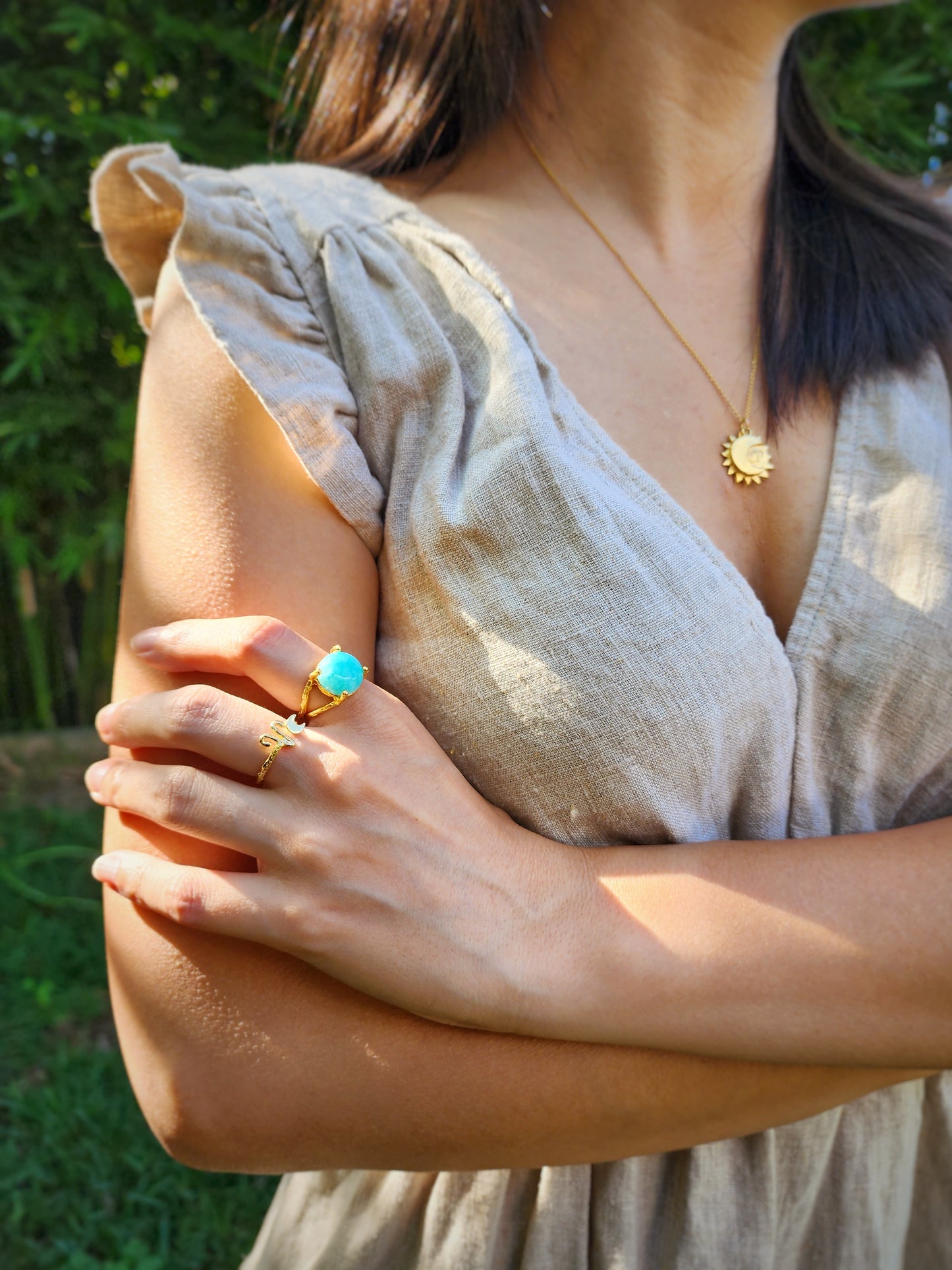 A woman in a taupe linen dress wearing a handmade 12mm natural Amazonite ring, styled with an Aries astrology ring and necklace. Photographed among native Australian greenery in a Sydney backyard, the hand-sculpted gold branch textures catch the dappled light, highlighting the piece’s raw elegance.