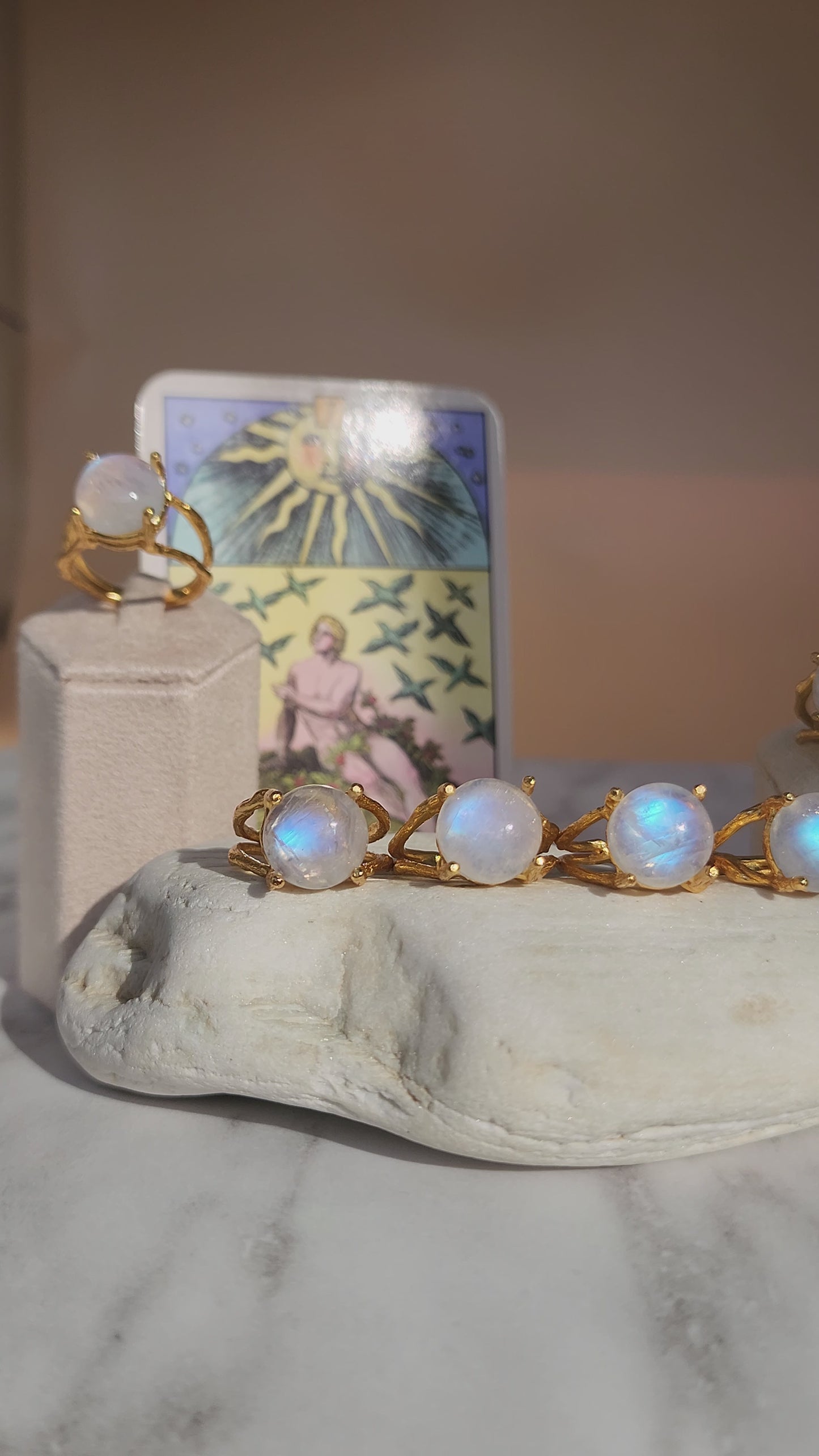Video of multiple natural moonstone rings handmade in 20k fine gold plate, shown styled on a white stone and tarot cards to highlight the celestial inspiration behind the lost wax made jewellery.