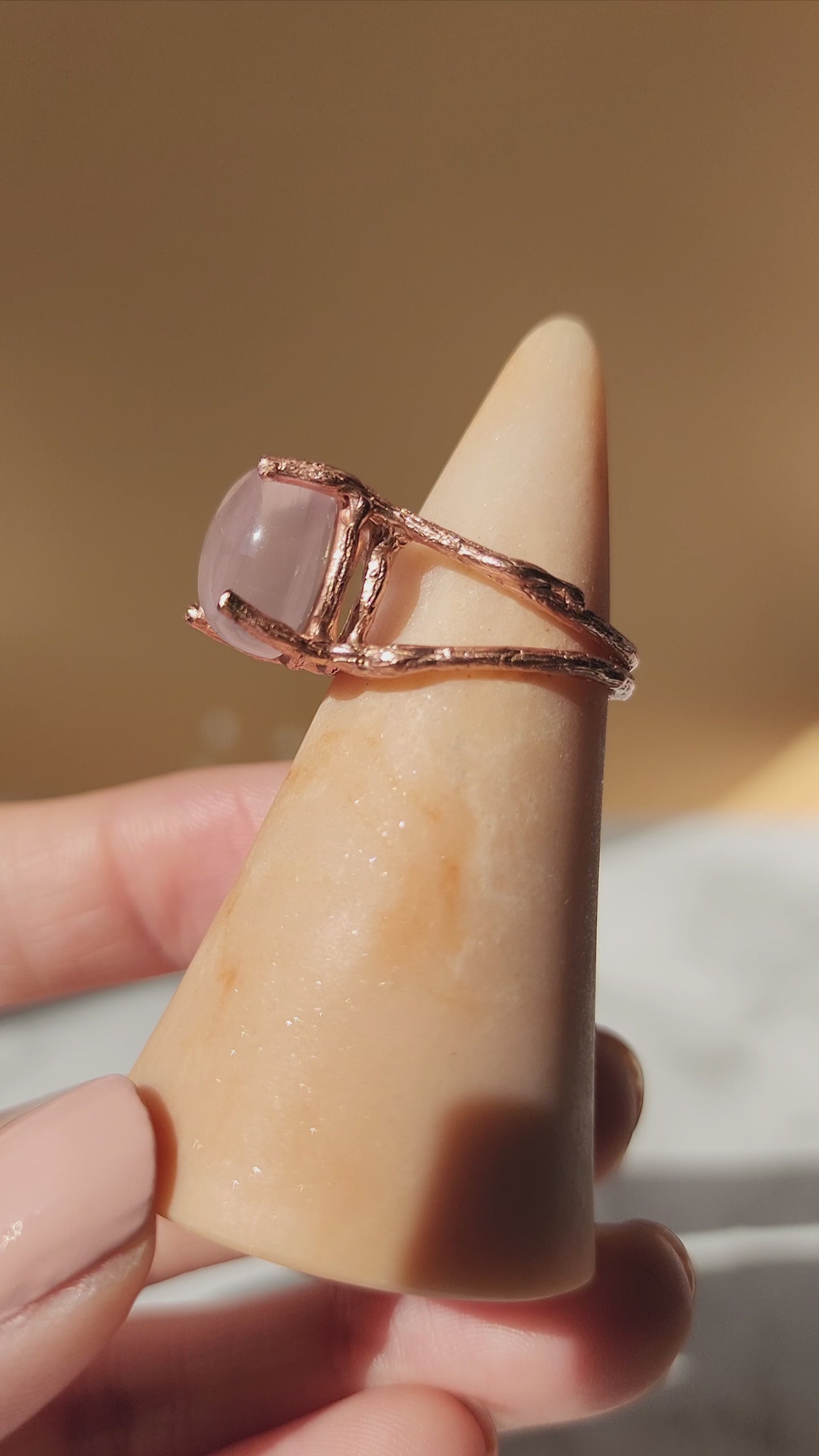A 20k fine gold plated rose gold ring featuring a rose gold gemstone is shown from the side to highlight the organic molten textures of the double gallery ring band. Gently panning to the front to show the 12mm round natural crystal that shines in the sunlight. 