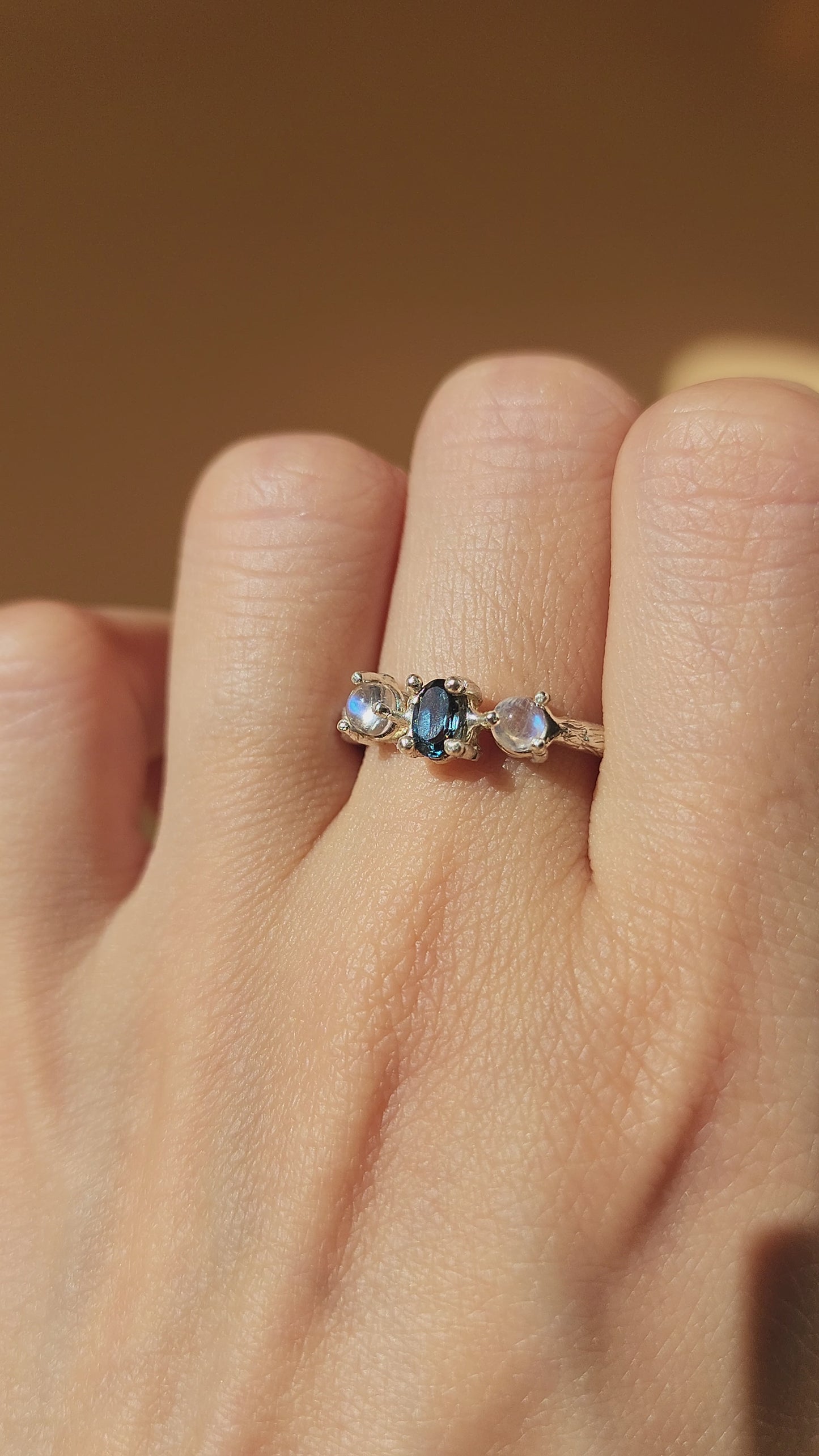 Hand-sculpted Blue Topaz ring with Moonstone accents, close-up video revealing the molten textures and brilliant gemstone clarity in the sun. Crafted in sterling silver, this artisanal ring demonstrates a unique, one-of-a-kind glow with every movement.
