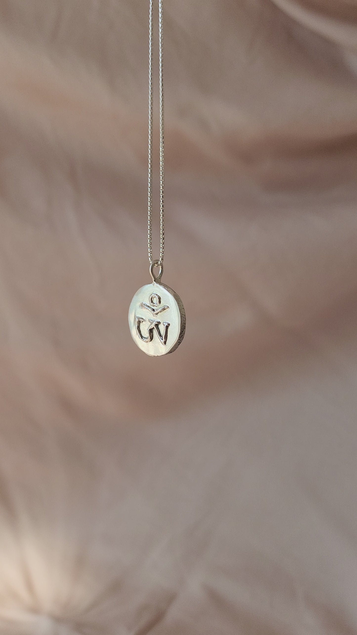 Hand-sculpted Tibetan Om pendant in polished sterling silver, viewed from the side to reveal its bold dimensional form. Defined by molten textures of the 3D carved Om symbol, this statement piece brings an atmospheric, old-world soul to a modern wardrobe.