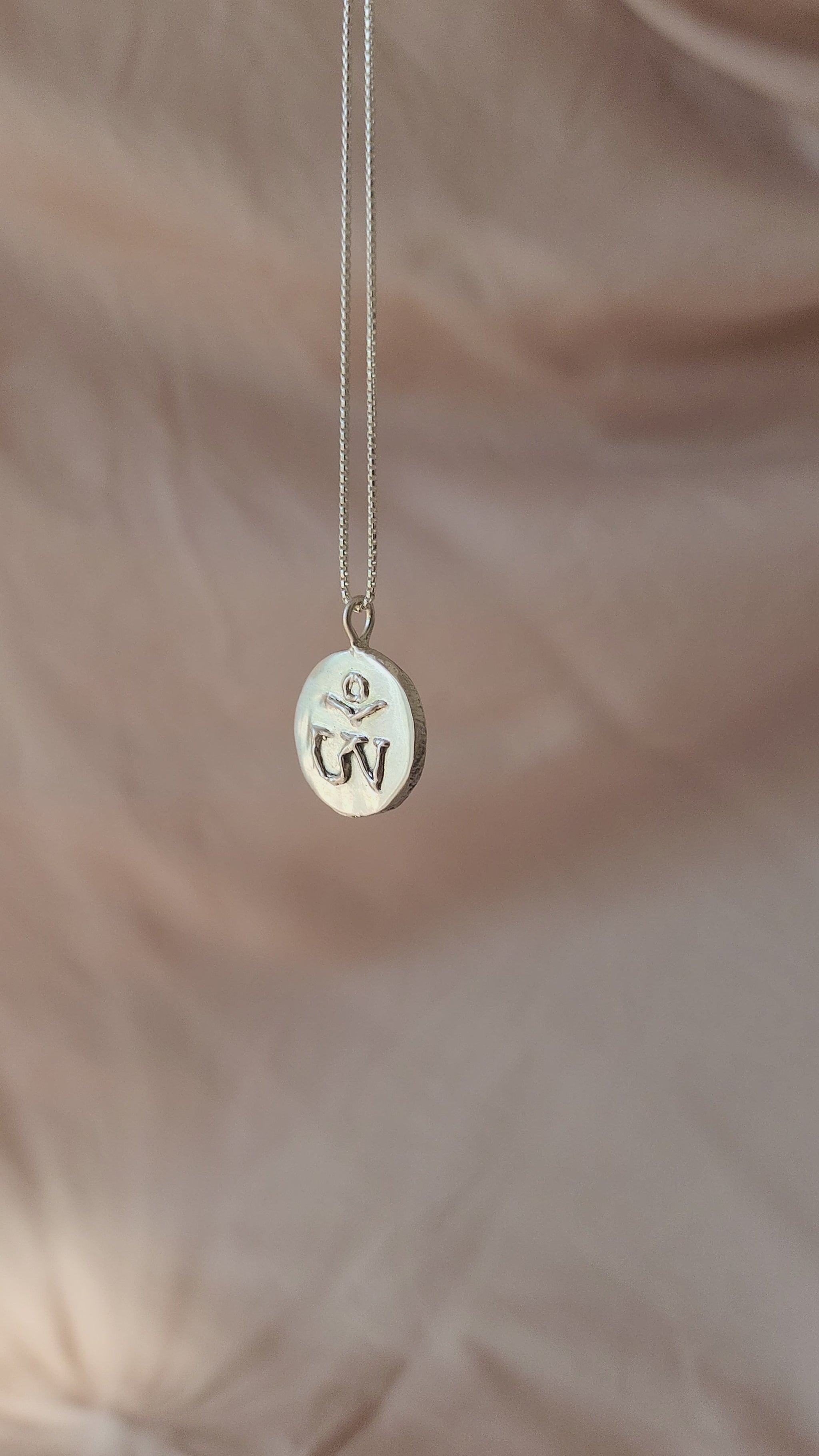 Hand-sculpted Tibetan Om pendant in polished sterling silver, viewed from the side to reveal its bold dimensional form. Defined by molten textures of the 3D carved Om symbol, this statement piece brings an atmospheric, old-world soul to a modern wardrobe.