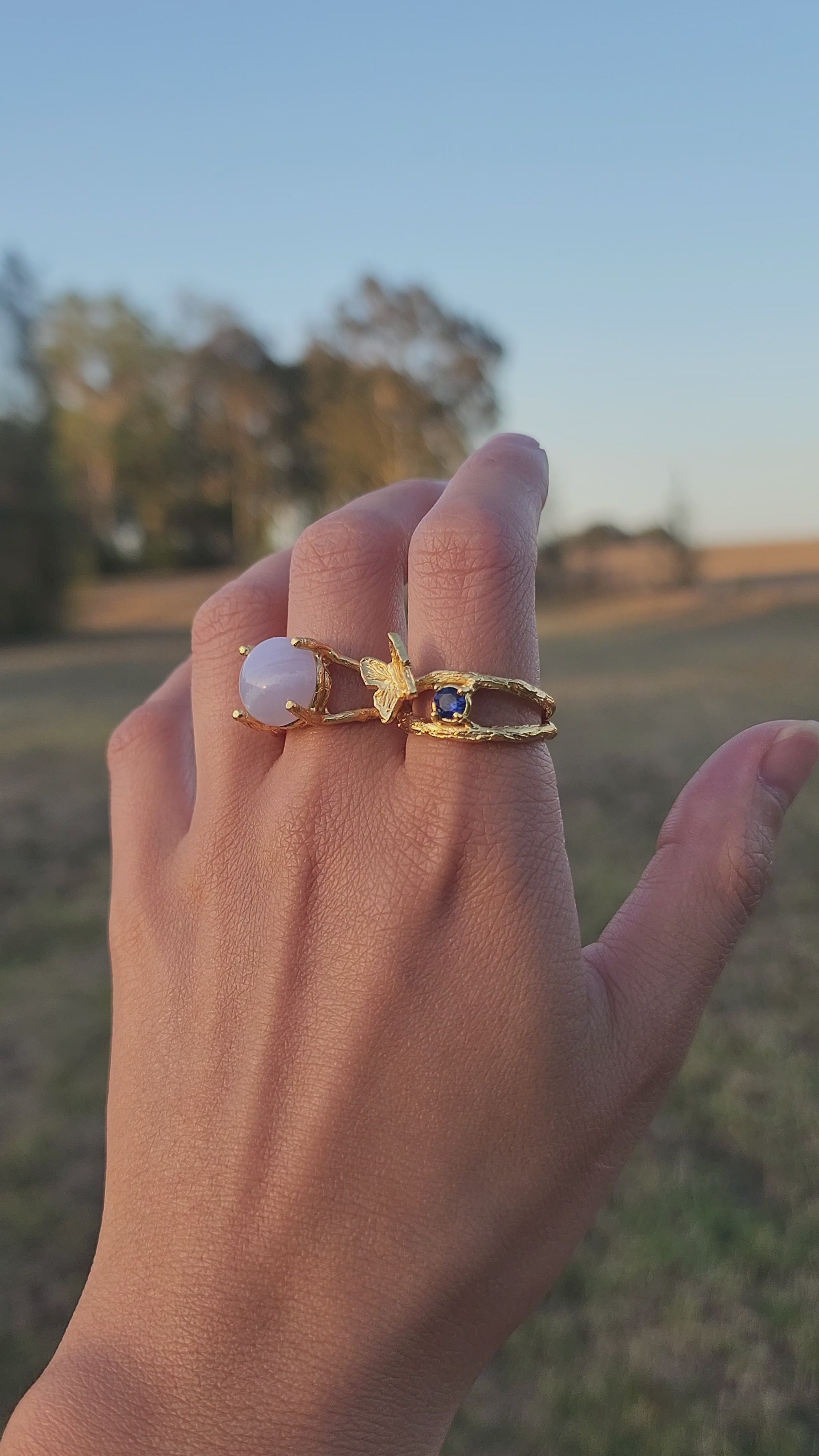 Hand wearing blue lace agate ring and sapphire ring, gently moving to showcase the textures and size of the statement rings. Shot in an Australian bush setting.