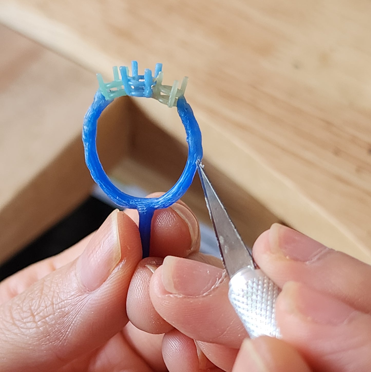 Close up of hands sculpting a ring using blue jewellers wax, showcasing the intricate details and textures of the lost wax process.